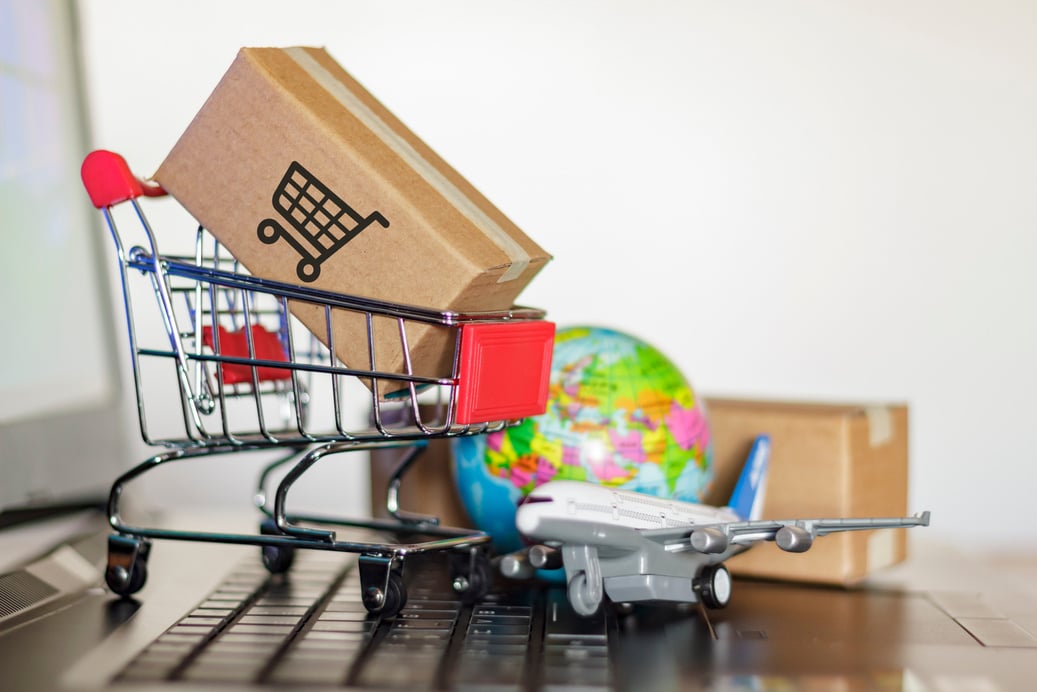 Shopping cart with cartons, globe and airplane on computer. Online shopping, e-commerce and worldwide delivery business concept